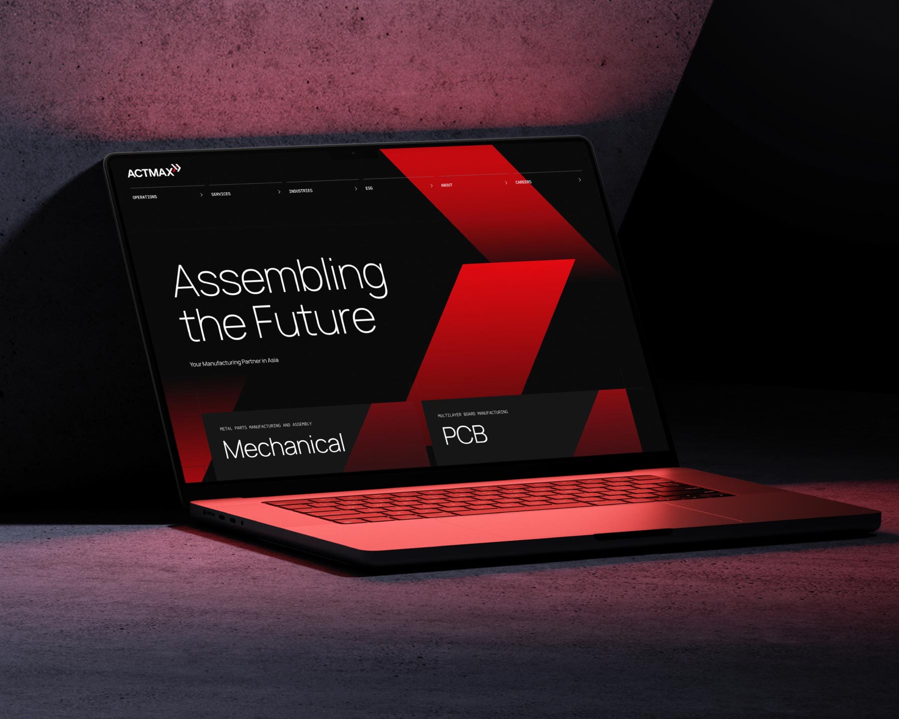 A laptop displaying the Actmax corporate website with bold red geometric designs. The laptop is placed on a textured concrete surface, highlighting an industrial web design created by Bike Bear.