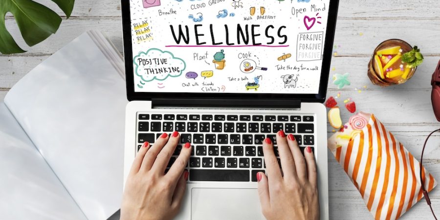 The image shows a woman's hands on laptop keyboard, the screen displaying info about wellness